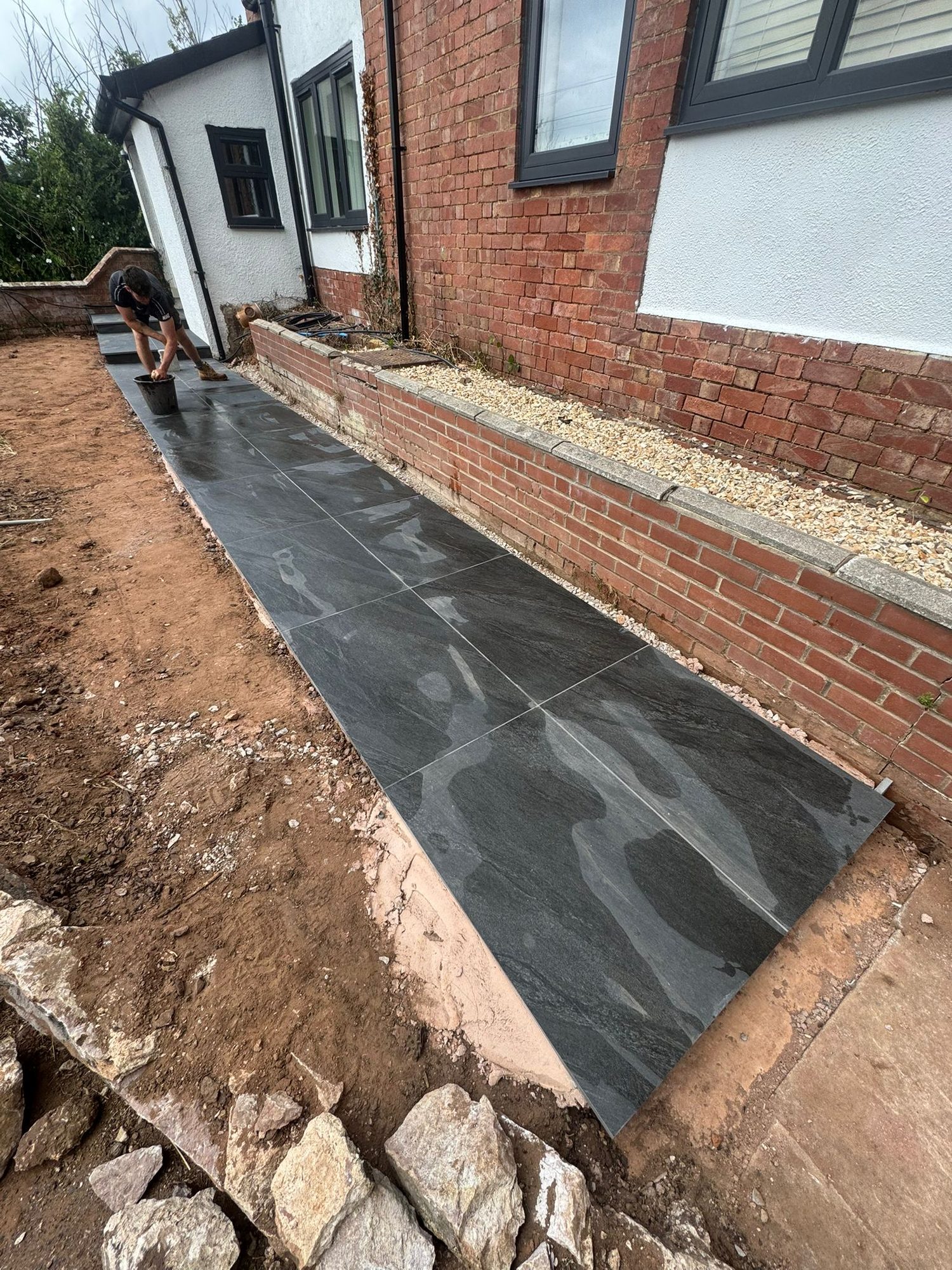 Dark porcelain paving laid alongside a brick retaining wall and rendered house