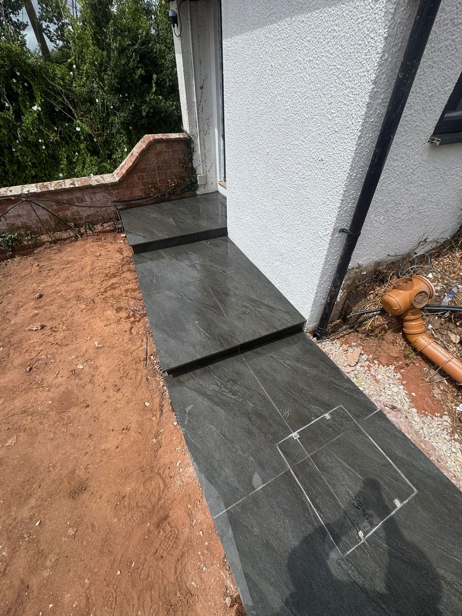 Dark grey porcelain paving and step laid to fall alongside a rendered wall