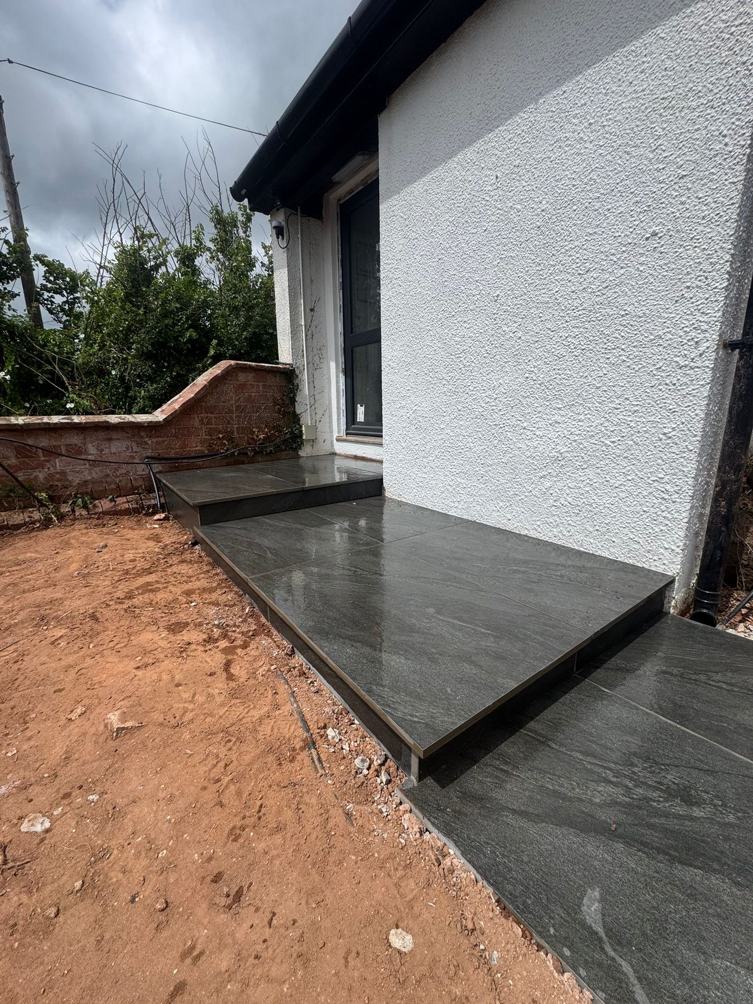 Dark porcelain patio and step formed against a rendered house wall