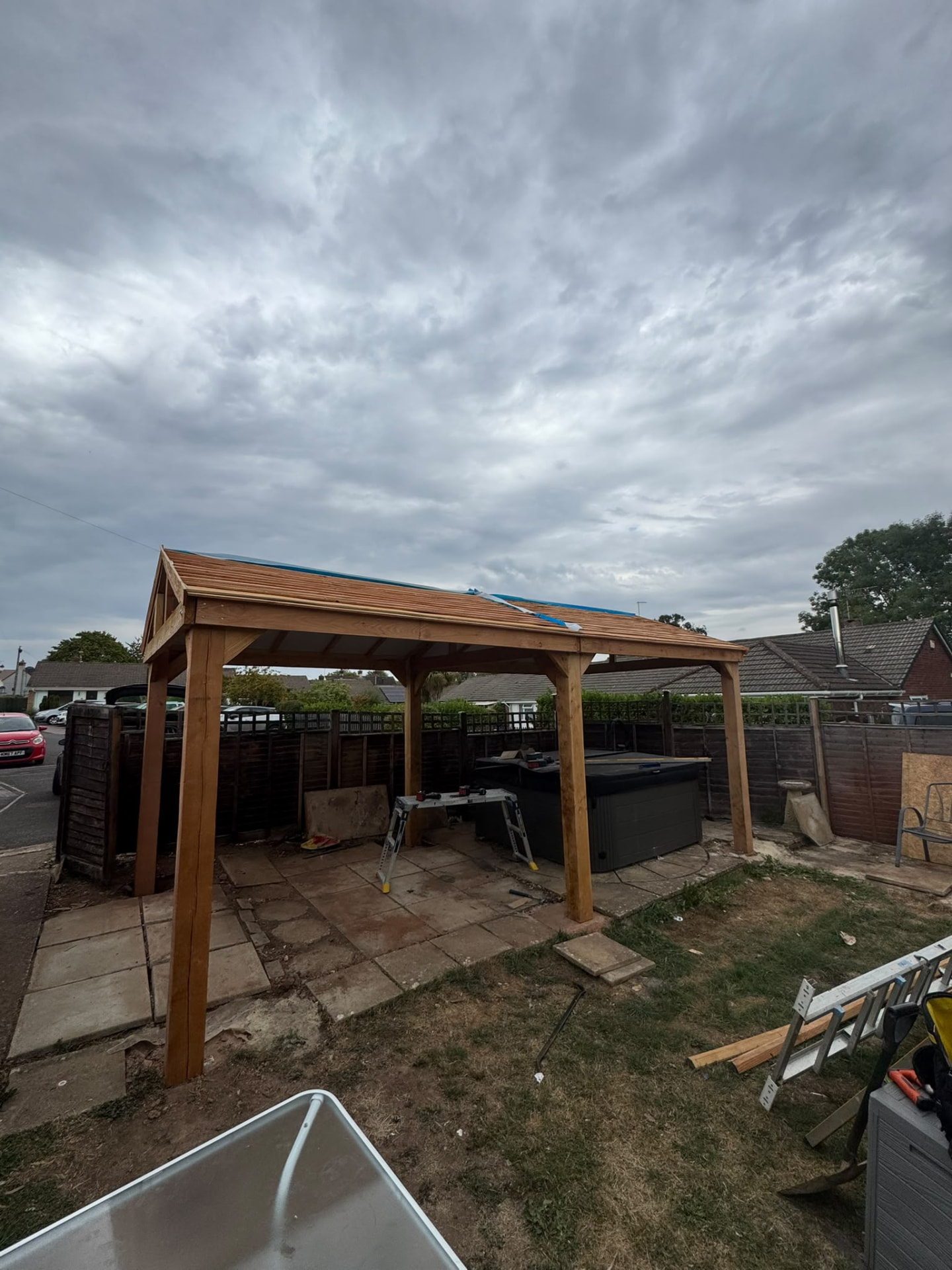Oak framed gazebo with pitched shingle roof built over a hot tub on a paved patio area