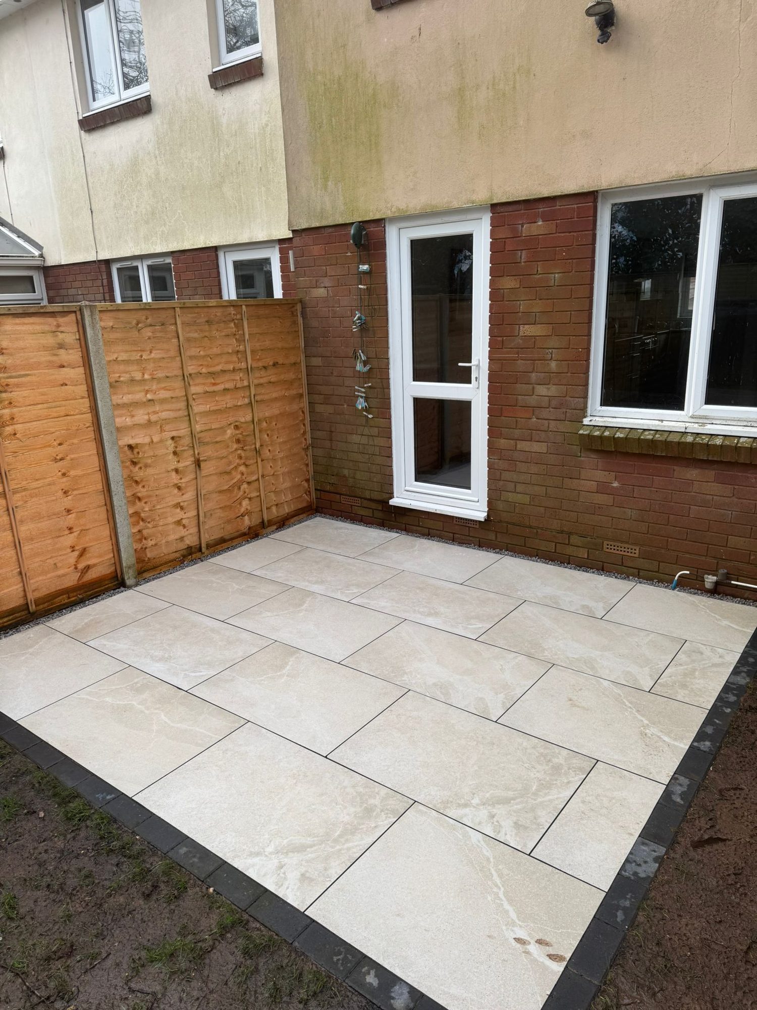 Cream porcelain patio with charcoal block border laid outside a back door