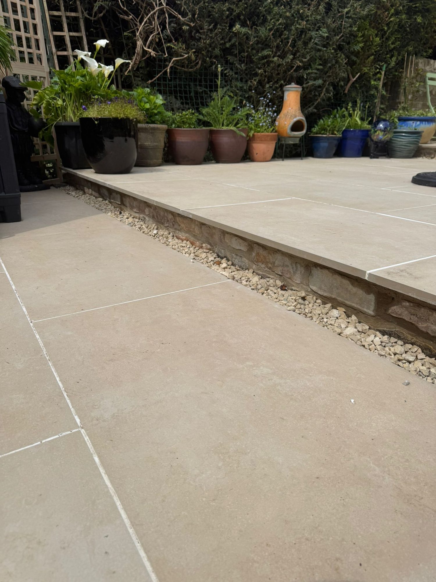 Raised porcelain patio with a gravel drainage margin and potted planting alongside