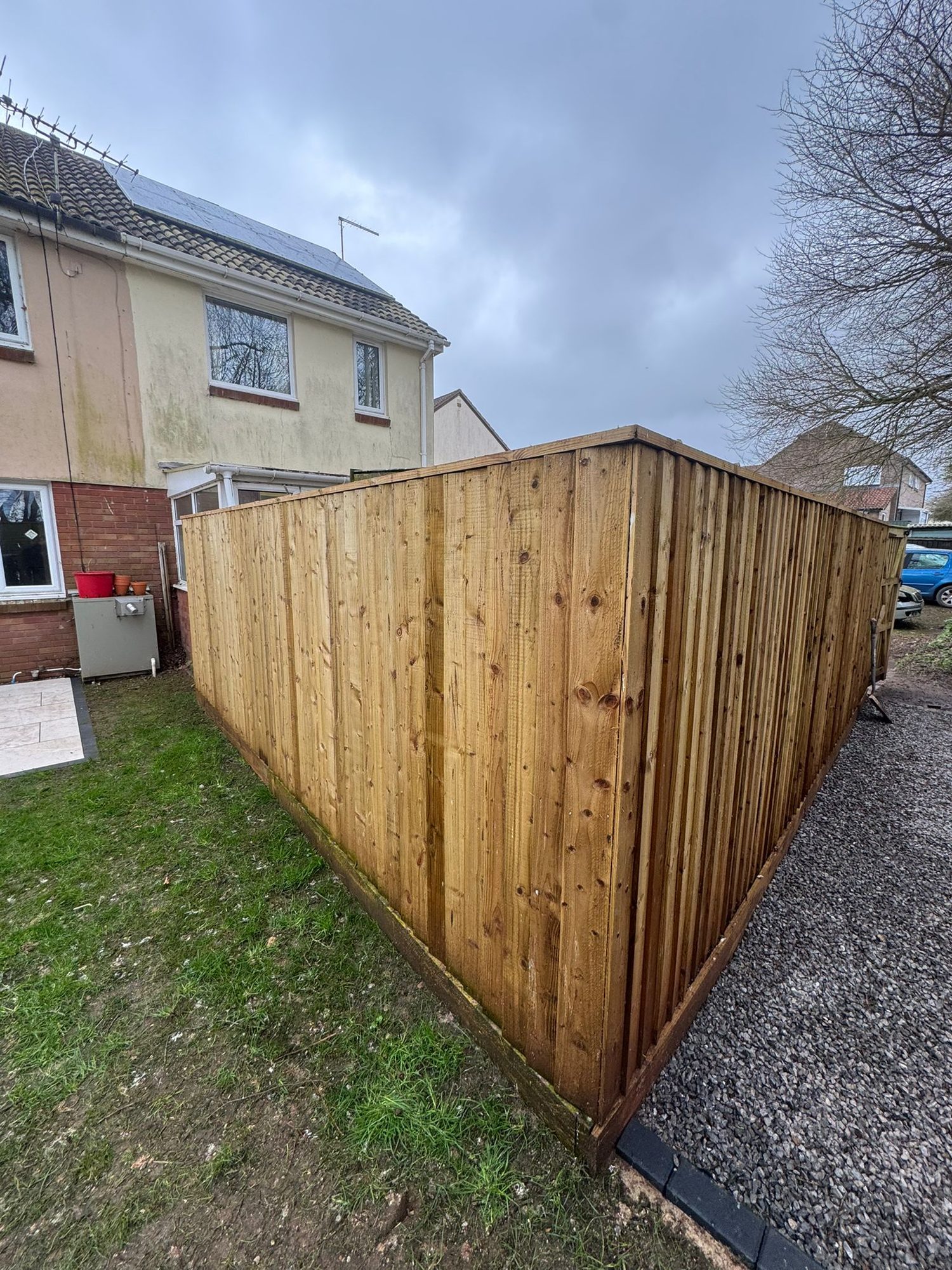 Tall timber fence enclosing a lawn and gravel path beside a house