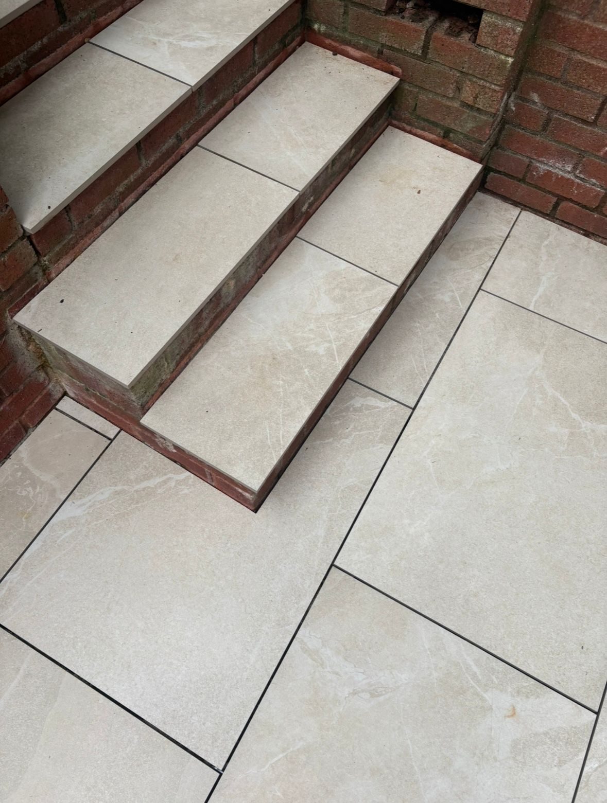 Porcelain paved steps with brick risers leading down to a patio