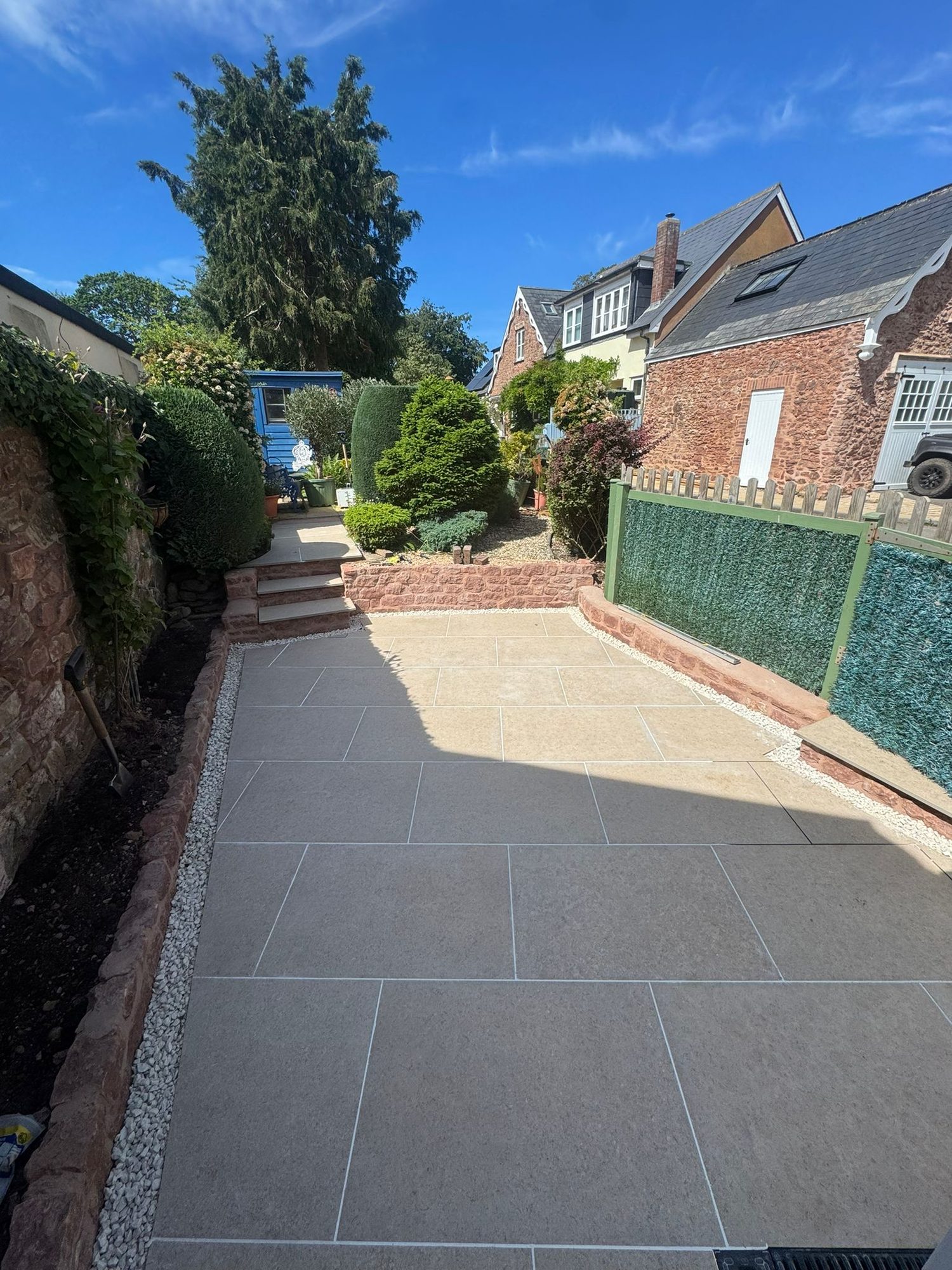 Two tone porcelain patio with red sandstone walling and white gravel margins