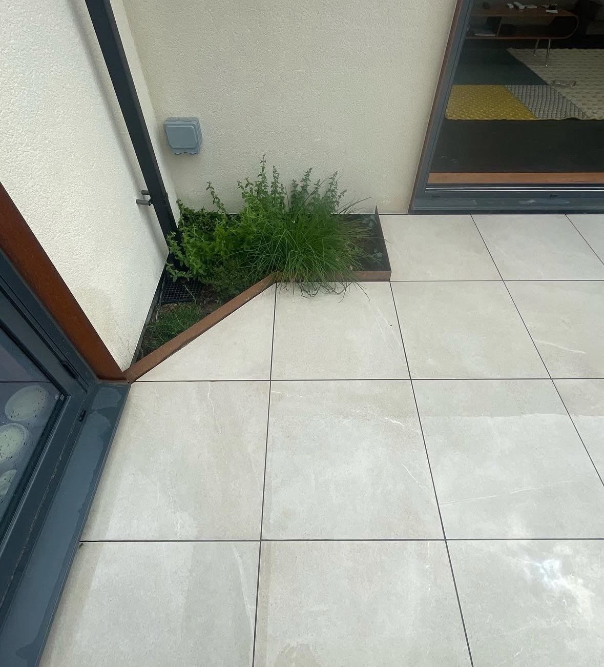 Large format porcelain paving cut neatly around a planted bed beside modern doors