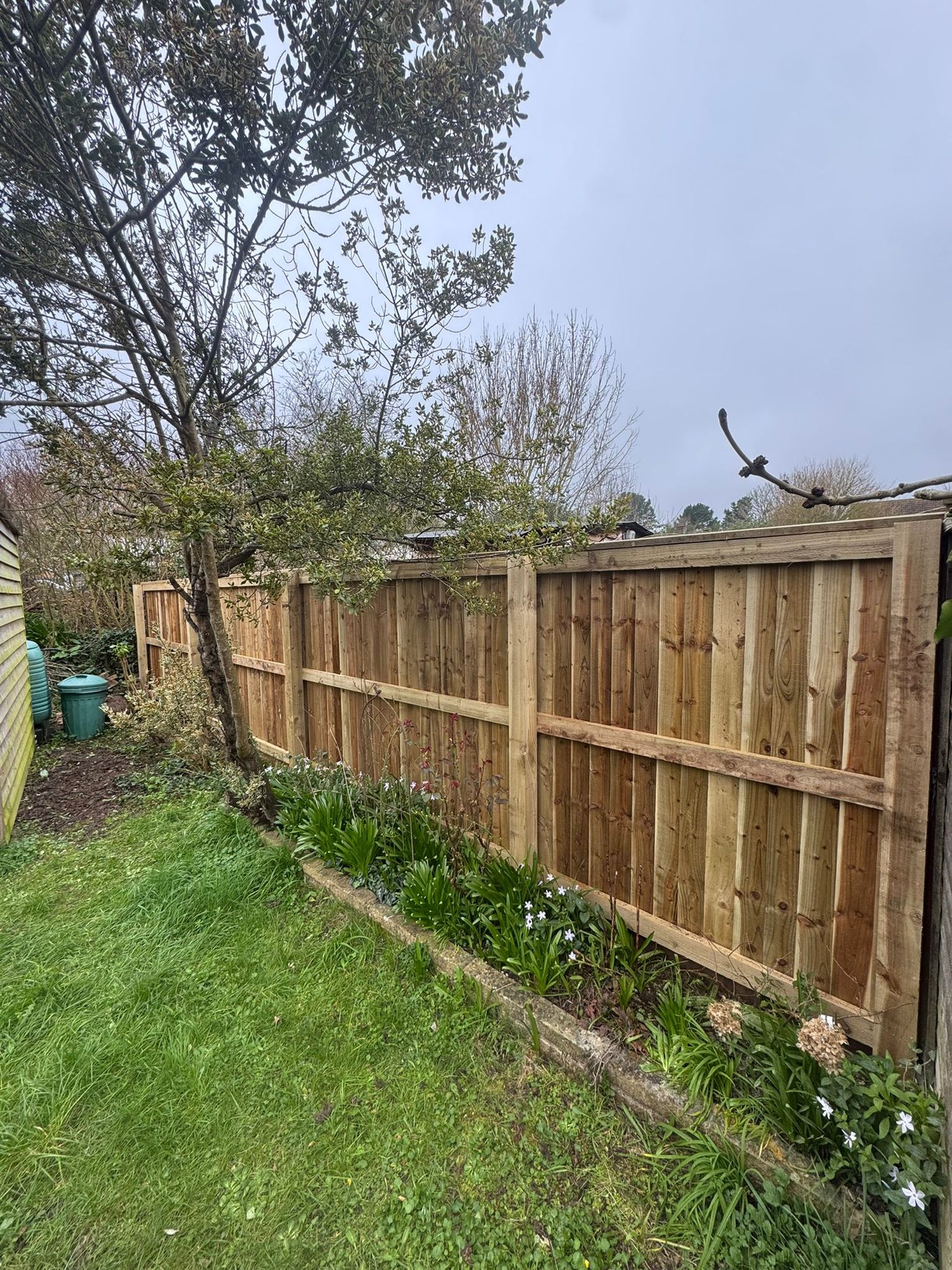 Timber garden fencing running alongside a planted border and mature trees