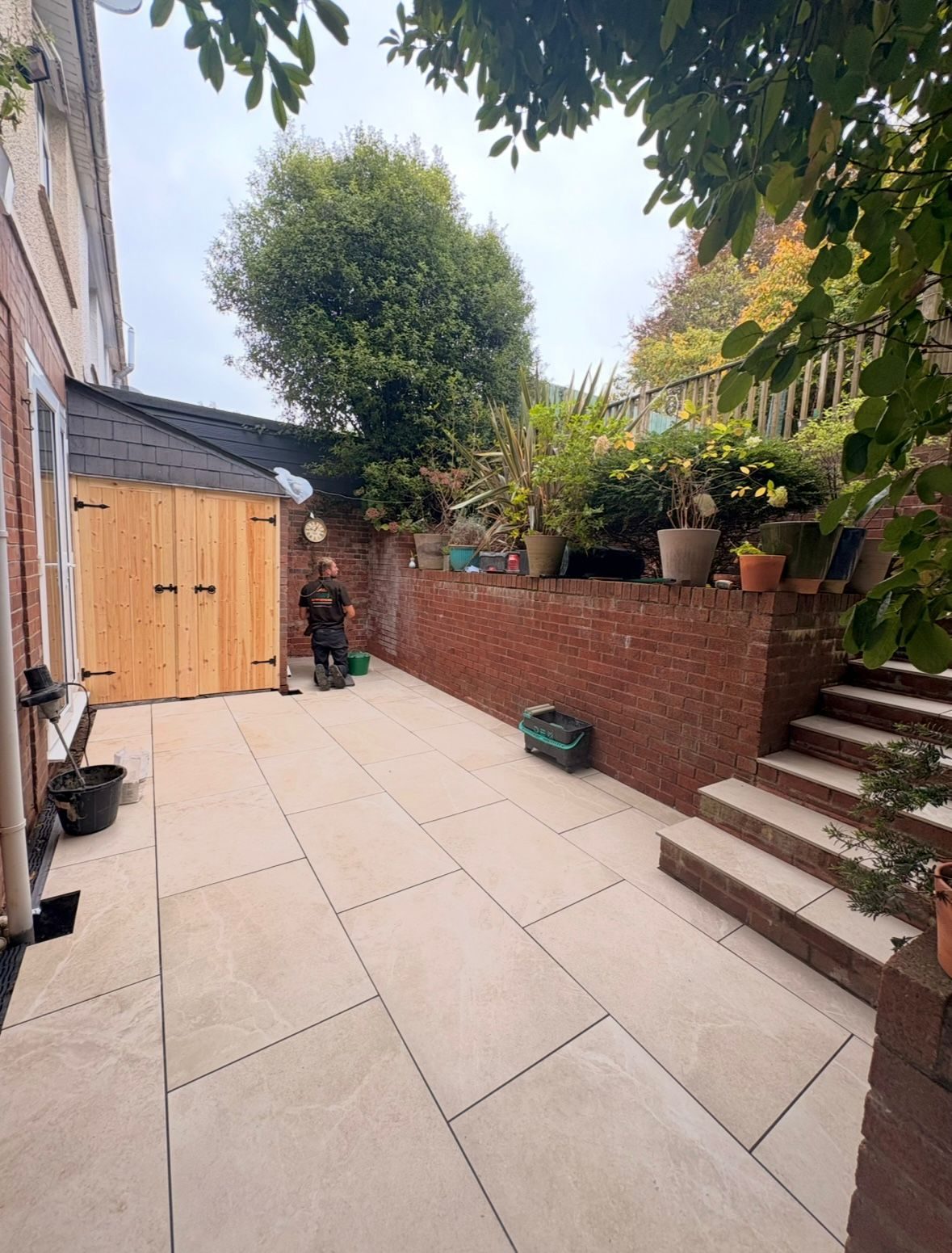 Cream porcelain courtyard paving laid between a brick wall and timber garage doors
