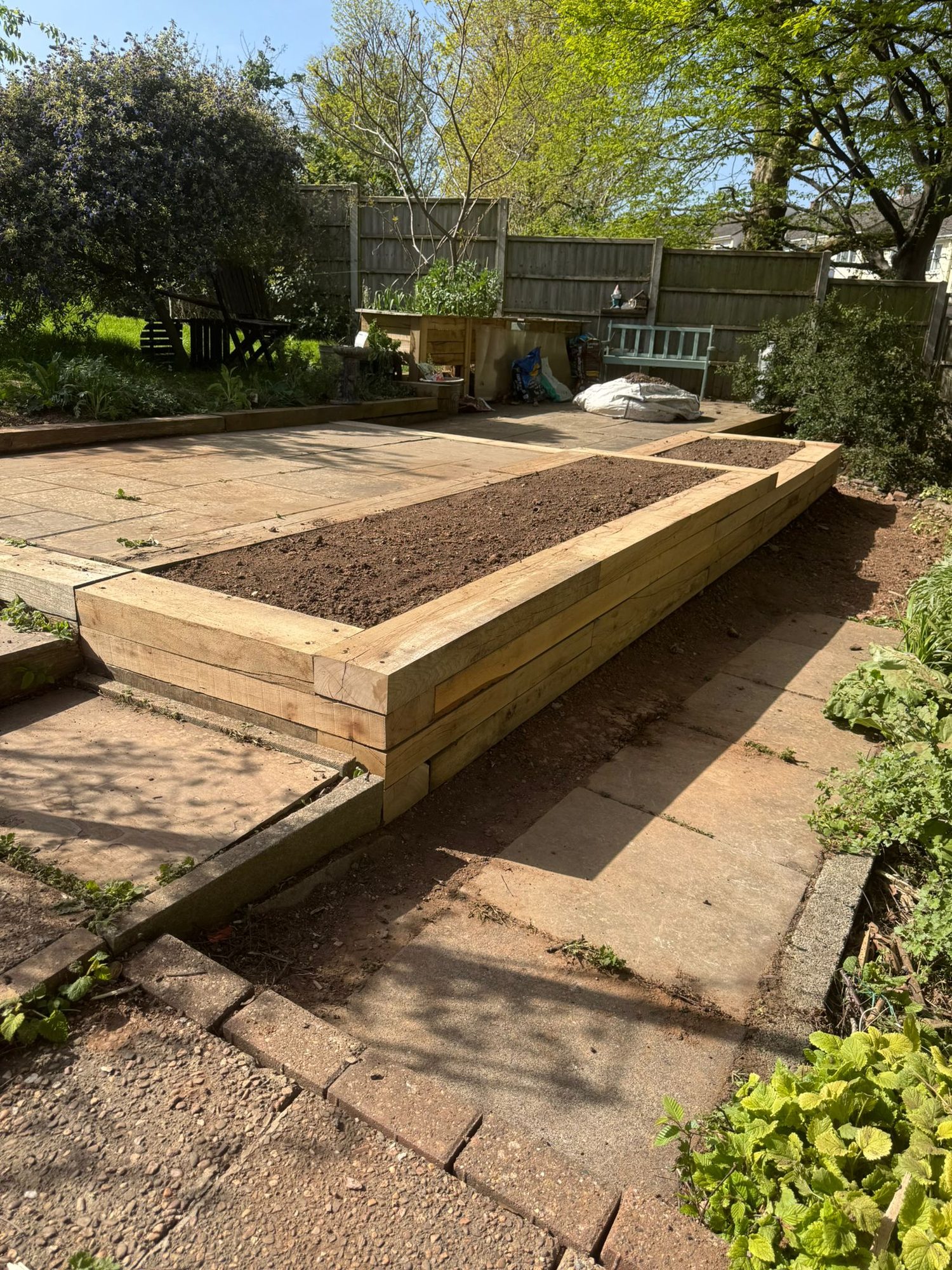 Timber sleeper raised bed filled with topsoil alongside existing garden paving